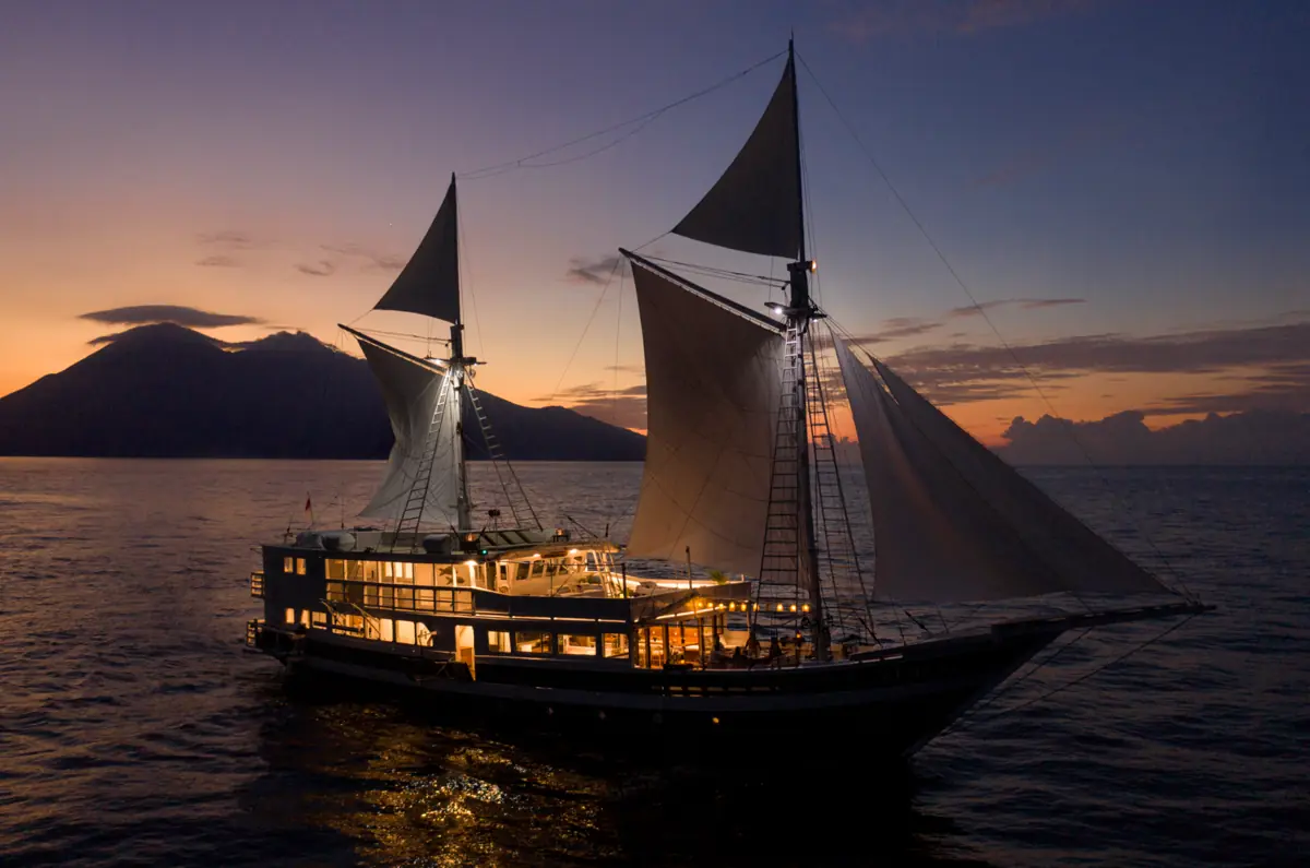Aliikai Voyage phinisi yacht glowing at sunset while anchored in Komodo National Park.