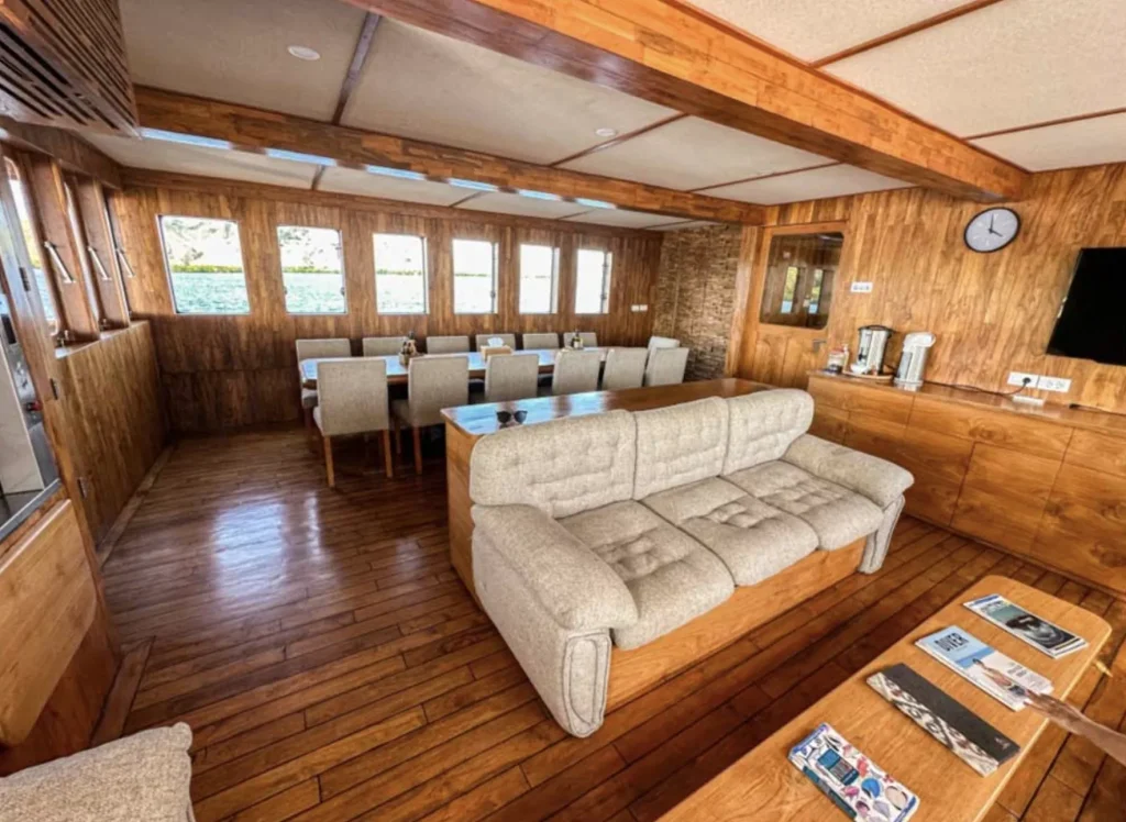 Indoor lounge and dining space on Komodo Sea Dragon yacht with wood interiors and cushioned seating.