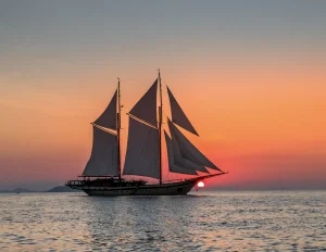 Lamima phinisi yacht sailing at sunset in Komodo National Park with glowing skies.