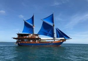 Moana phinisi yacht sailing with vibrant blue sails across the waters of Komodo National Park