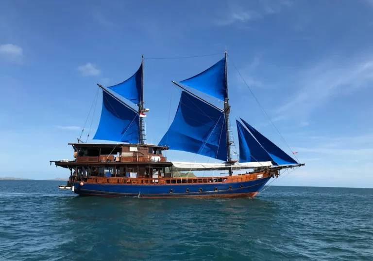Moana phinisi yacht sailing with vibrant blue sails across the waters of Komodo National Park